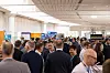 Dicht gefülltes Bordnetzkongress-Messefoyer mit Geschäftsleuten vor mehreren Firmenständen. Auf einem steht Automotive Digital Transformation.