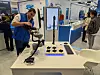 Mann richtet kollaborativen Roboterarm an einem Messestand mit Technikaufbau aus.
