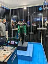 Messestand mit grün leuchtendem Robotersystem, Monitoren und Messebesuchern im Hintergrund.