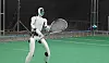 Humanoider Roboter mit Tennisschläger auf einem grünen Indoor-Tennisplatz in Spielhaltung.