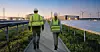 Zwei Personen in Warnwesten gehen zwischen Solarmodulen und Windrädern in einem Energiefeld.