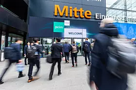 Menschen gehen vor dem Eingang einer Messehalle mit „Mitte“-Schriftzug und „welcome“-Banner.