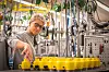 Mitarbeiter montiert gelbe Bauteile an einer Produktionslinie mit Kabeln und Maschinen in einer Fertigungshalle.
