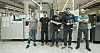 Fünf Männer stehen in einer Produktionshalle vor Maschinen und halten Leiterplatten oder Bauteile in den Händen.