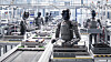 Humanoide Roboter stehen an Förderbändern in einer hellen Produktionshalle.