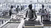 Humanoide Roboter stehen an Förderbändern in einer hellen Produktionshalle.