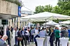 Teilnehmer des 30. AUTOMOBIL-ELEKTRONIK Kongresses 2026 stehen im Außenbereich des Forums am Schlosspark in Ludwigsburg und nutzen die Kongresspause für Gespräche und Networking. Unter großen weißen Sonnenschirmen und an Stehtischen unterhalten sich zahlreiche Besucher in Businesskleidung, viele tragen blaue Lanyards mit Namensschildern. Im Hintergrund sind das Kongressgebäude, Bäume, Cateringbereiche und weitere Teilnehmer zu sehen. Die Aufnahme zeigt die Pausenatmosphäre des AEK, den persönlichen Austausch zwischen Fachbesuchern, OEMs, Zulieferern, Halbleiterunternehmen und Technologiepartnern sowie den Außenbereich des AUTOMOBIL-ELEKTRONIK Kongresses in Ludwigsburg. Das Bild eignet sich für Beiträge über Networking, Branchentreff, Automotive-Community, Fachkongress, AEK 2026, Kongresspausen, persönliche Gespräche, Automotive Electronics, Software-defined Vehicles und KI im Fahrzeug.