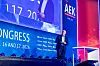 Glen de Vos, CEO von MicroVision, steht auf der Bühne des 30. AUTOMOBIL-ELEKTRONIK Kongresses 2026 in Ludwigsburg und hält einen Vortrag zu „Lidar 2.0“ im Rahmen des Formats „Technologies to Watch“. Er trägt einen dunklen Anzug, ein helles Hemd und eine Brille, spricht mit Headset-Mikrofon und hält einen Presenter in der Hand. Im Hintergrund ist die blau-rote Bühne mit AEK-Branding, Sponsorlogos und großem Kongressschriftzug zu sehen, darüber erscheint der Speaker zusätzlich auf der großen Leinwand. Das Bild eignet sich für Beiträge über Glen de Vos, MicroVision, Lidar 2.0, Fahrzeugsensorik, automatisiertes Fahren, Level 3, multimodale Wahrnehmung, Kamera, Radar, Lidar, Solid-State-Lidar, Automotive-Grade-Sensoren, Software-defined Vehicles, ADAS, Sensorarchitekturen und den AUTOMOBIL-ELEKTRONIK Kongress in Ludwigsburg.