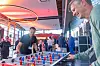 Zwei Teilnehmer spielen beim 30. AUTOMOBIL-ELEKTRONIK Kongress 2026 in Ludwigsburg an einem Tischkicker im Foyer. Im Vordergrund sind die roten und blauen Spielfiguren des Kickertischs scharf zu sehen, links steht ein Teilnehmer im schwarzen FEV-Poloshirt, rechts ein weiterer Teilnehmer im hellgrünen Pullover. Im Hintergrund unterhalten sich weitere Kongressgäste in entspannter Atmosphäre, während warmes Licht und große Fenster den Networking-Bereich prägen. Das Bild zeigt die informelle Seite des AEK mit Austausch, Spiel, Pause und persönlicher Begegnung zwischen den Sessions. Es eignet sich für Beiträge über Networking, Kongresspausen, Teilnehmererlebnis, Community, Foyer-Atmosphäre, Rahmenprogramm und den AUTOMOBIL-ELEKTRONIK Kongress in Ludwigsburg.