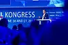Christian Sobottka, President und CEO von Harman sowie President Harman Automotive, steht auf der Bühne des 30. AUTOMOBIL-ELEKTRONIK Kongresses 2026 in Ludwigsburg und hält einen Vortrag mit dem Titel „Differentiating Experiences at Speed and Scale“. Er trägt einen dunklen Anzug, ein helles Hemd und ein Headset-Mikrofon, steht hinter einem weißen Rednerpult und hält einen Presenter in der Hand. Im Vordergrund sind unscharf mehrere Personen aus dem Publikum zu sehen, wodurch der Blick auf die blau ausgeleuchtete Bühne und den Speaker gelenkt wird. Im Hintergrund erscheinen das Branding des AUTOMOBIL-ELEKTRONIK Kongresses, das Veranstaltungsdatum 16. und 17. Juni 2026 sowie Sponsorenlogos wie Microsoft, Qualcomm, Synopsys, Texas Instruments und T-Systems. Die Aufnahme eignet sich für Beiträge über Christian Sobottka, Harman Automotive, Harman, Samsung, Automotive User Experience, differenzierende Fahrzeugerlebnisse, Cockpit der Zukunft, KI im Innenraum, AI-orchestrated Experience, zentrale Compute-Plattformen, Software-defined Vehicles, AI-defined Vehicles, ADAS-Integration, Audio im Auto, Displays, Konnektivität, Kontextdaten, intelligente Interaktion, Consumerization im Automobil, digitale Ökosysteme, China als Innovationstreiber, Geschwindigkeit in der Fahrzeugentwicklung, Produktisierung, Software Factory, SOP in 52 Wochen, Automotive-Partnerschaften und den AUTOMOBIL-ELEKTRONIK Kongress in Ludwigsburg.
