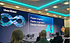 Konferenzbühne mit großer LED-Wand, Beamer und Publikum im Vordergrund.