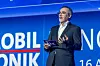 Alfred Vollmer steht auf der Bühne des 30. AUTOMOBIL-ELEKTRONIK Kongresses 2026 in Ludwigsburg und hält die Abschlussworte der Veranstaltung. Er trägt einen dunklen Anzug, ein weißes Hemd, eine Brille und ein Headset-Mikrofon und hält Moderationskarten mit dem AEK-Logo in der Hand. Im Hintergrund ist die blau ausgeleuchtete Bühnenwand mit großem AUTOMOBIL-ELEKTRONIK Kongress-Branding und Teilen der Datumsangabe 16. und 17. Juni zu sehen. Das Bild eignet sich für Beiträge über Alfred Vollmer, die Abschlusszusammenfassung des AUTOMOBIL-ELEKTRONIK Kongresses, den Rückblick auf zwei Kongresstage, AI-defined Vehicle, Software-defined Vehicle, Chiplets, S-CORE, Edge AI, 48-V-Architekturen, Open Source, Fahrzeugsoftware, Automotive E/E-Architekturen, Automotive Software, das AEK-Netzwerk, die Automobilindustrie in Ludwigsburg und den Termin des AUTOMOBIL-ELEKTRONIK Kongresses 2027 am 22. und 23. Juni.