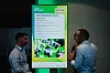Zwei Personen betrachten ein großes, beleuchtetes Informationsdisplay mit Nachhaltigkeitsthema.