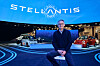 Ned Curic, EVP, Chief Engineering Officer and CTO bei Stellantis, sitzt auf einem Hocker vor dem blau beleuchteten Stellantis-Messestand mit großem Stellantis-Logo und mehreren ausgestellten Fahrzeugen. Das Bild zeigt Curic in einem dunklen Pullover über einem Hemd vor einer modernen Automotive-Inszenierung mit Fahrzeugen, Lichtlinien und digitalen Displays. Das Motiv passt zu einem Interview über Stellantis, Software-defined Vehicle, STLA Brain, STLA SmartCockpit, digitale Fahrzeugarchitekturen, Customer Experience, Cockpit-Bedienung, Personalisierung, globale Softwareplattformen, regionale Anforderungen, Markenidentität, vernetzte Dienste, Fahrzeugsoftware, Automotive Electronics und die Frage, wie digitale Funktionen im Auto einfacher und kundenorientierter gestaltet werden können.