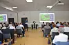 Publikum sitzt in einem Konferenzraum und blickt auf eine Präsentation mit projizierten Folien.