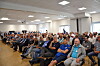Voll besetzter Konferenzraum mit vielen sitzenden Zuhörern in einem hellen Saal.