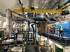 Blick in eine technische CERN-Galerie während der Long Shutdown 3 des Large Hadron Collider: Zu sehen sind ein gelber Deckenkran, große silberne Rohrleitungen, Lüftungskanäle, Kabeltrassen, blaue Schaltschrankreihen, Arbeitsplattformen und mehrere Techniker mit Helmen und Warnwesten. Das Bild zeigt die industrielle Infrastruktur, die für den Umbau des LHC zum High-Luminosity LHC erneuert und erweitert wird. Im Mittelpunkt stehen nicht die Teilchenkollisionen selbst, sondern die technischen Systeme hinter dem Forschungsbetrieb: Stromversorgung, Kühlung, Kryotechnik, Steuerungstechnik, Sicherheitssysteme und Servicebereiche. Die Szene verdeutlicht, dass der LHC-Umbau ein komplexes Engineering-Projekt ist, bei dem Beschleunigertechnik, Elektronik, Datenverarbeitung und Infrastruktur zusammenwirken müssen, damit ATLAS und CMS ab 2030 deutlich höhere Kollisionsraten auswerten können.