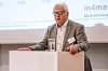 Ein älterer Mann spricht an einem Rednerpult vor einer Leinwand mit Präsentation.