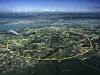 Luftaufnahme der Region um Genf mit eingezeichneter gelber Ringstruktur des Large Hadron Collider am CERN. Der 27 Kilometer lange LHC-Ring verläuft unterirdisch durch die französisch-schweizerische Grenzregion, unter Feldern, Ortschaften und Infrastruktur nahe dem Genfer See und den Alpen. In der Grafik sind zentrale Standorte des Beschleunigerkomplexes markiert, darunter CMS auf der französischen Seite bei Cessy, ATLAS am CERN-Standort Meyrin nahe Genf, ALICE, der SPS-Vorbeschleuniger sowie die CERN-Standorte Meyrin und Prévessin. Das Bild verdeutlicht die enorme räumliche Dimension des Teilchenbeschleunigers: Die Experimente ATLAS und CMS liegen mehrere Kilometer voneinander entfernt an eigenen Kollisionspunkten im unterirdischen Ring. Für den Umbau zum High-Luminosity LHC werden nicht nur Komponenten im Beschleunigertunnel modernisiert, sondern auch die Detektoren und ihre Elektronik, darunter Sensoren, Auslesekanäle, Trigger-Systeme, Datenübertragung, Stromversorgung und Kühlung.