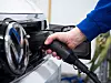 Hand steckt Ladekabel in die Ladebuchse eines weißen Elektroautos.