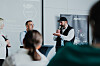 Diskussionsrunde in einem Konferenzraum mit Publikum und Präsentationswand.