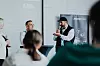 Diskussionsrunde in einem Konferenzraum mit Publikum und Präsentationswand.
