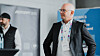 Mann im Anzug steht vor Konferenzbanner mit weiterer Person im Hintergrund.