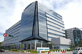 Modernes Bürogebäude mit Glasfront an einer Straße, davor ein Wistron-Schild und einige Fahrzeuge.