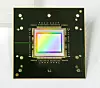 Schwarze Leiterplatte mit zentralem Mikrochip und farbigem Testmuster auf hellem Hintergrund.