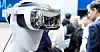 Humanoider Roboter mit Spiegel-Headset auf einer Messe, Menschen im Hintergrund.