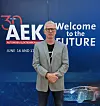 Mann im grauen Blazer steht vor einer blauen AEK-Messewand mit der Aufschrift „Welcome to the Future“.