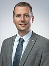 Mann im grauen Anzug mit Krawatte vor hellem Hintergrund.