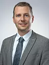 Mann im grauen Anzug mit Krawatte vor hellem Hintergrund.