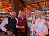 Vier Personen stehen in einer farbig dekorierten Bar und halten Getränke in der Hand.