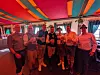 Gruppe von Menschen mit Getränken steht unter einem bunt gestreiften Zelt.
