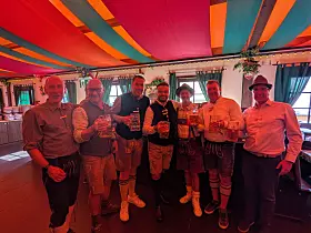 Gruppe von Menschen mit Getränken steht unter einem bunt gestreiften Zelt.