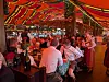 Belebtes Festzelt mit Menschen an Tischen unter einem rot-gelb gestreiften Zeltdach.
