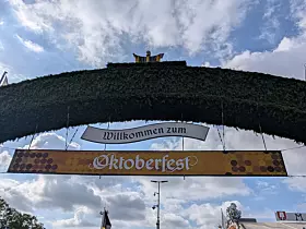 Grüner Eingangsbogen mit dem Schriftzug „Willkommen zum Oktoberfest“ vor blauem Himmel.