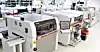 Automatisierte Maschinen und Monitore in einer hellen Industriehalle.
