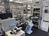 Industrieroboter in einer abgeschirmten Fertigungszelle mit Fördertechnik und Maschinensteuerung.