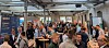 Menschen sprechen bei einem Networking-Event in einer großen Halle mit Stehtischen und Werbebannern.