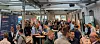 Menschen sprechen bei einem Networking-Event in einer großen Halle mit Stehtischen und Werbebannern.
