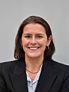 Lächelnde Frau im schwarzen Blazer vor grauem Hintergrund.