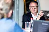 Nahaufnahme von Christoph Hartung, CTO Systems, Software and Services bei Bosch Mobility, während eines Interviews auf den ETAS Connections 2026 in Stuttgart. Hartung sitzt rechts im Bild, trägt eine dunkle Anzugjacke über einem weißen Hemd und eine rechteckige Brille. Er spricht und hebt dabei seine rechte Hand, um seine Ausführungen zu unterstreichen. Im linken Vordergrund ist ein Gesprächspartner mit zusammengebundenen Haaren und blauem Oberteil unscharf zu erkennen. Auf dem Tisch im Vordergrund befinden sich ein Trinkglas, eine Wasserflasche mit rotem Verschluss und ein aufgeklappter Laptop. Der Hintergrund ist durch die geringe Schärfentiefe weichgezeichnet.