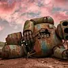 Ein ergreifendes Bild eines einst fortschrittlichen Roboters, der nun verlassen und verwittert in einer kargen Landschaft liegt. Der verrostete Metallkörper und die zerbrochenen Schaltkreise stehen für den Lauf der Zeit und den unaufhaltsamen Fortschritt bzw. Obsoleszenz. Der Himmel über dem Bild ist eine Mischung aus leuchtenden Rosa- und Orangetönen, die ein melancholisches Licht auf die Szene werfen.